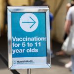 A blue direction sign inside a vaccination centre reads "Vaccinations for 5 to 11 year olds" with an arrow pointing to the right.