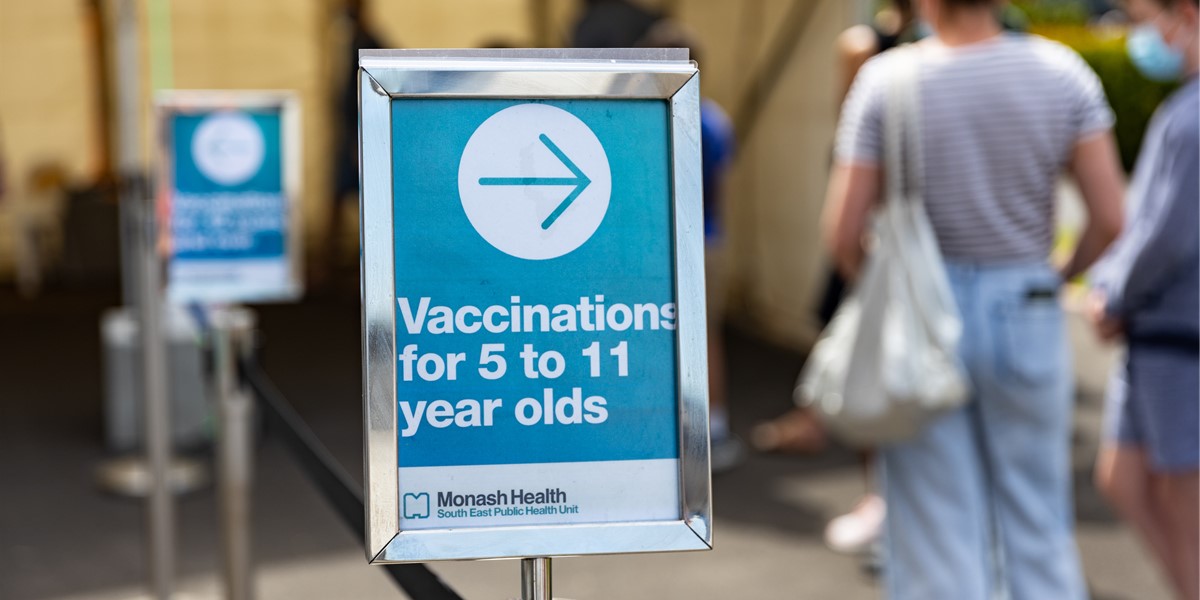 A blue direction sign inside a vaccination centre reads "Vaccinations for 5 to 11 year olds" with an arrow pointing to the right.